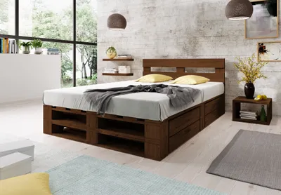 A bedroom scene featuring a wooden pallet bed with storage drawers, bedside table, and decorative elements.