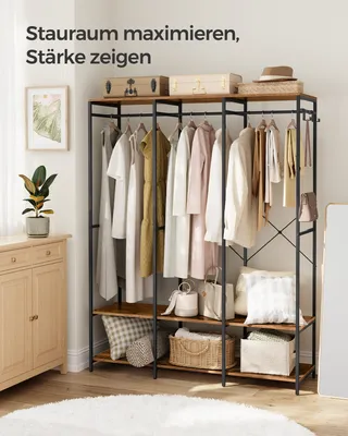A well-organized open wardrobe with clothes hanging on a rack and items stored on shelves below, set in a room with a dresser and a plant.