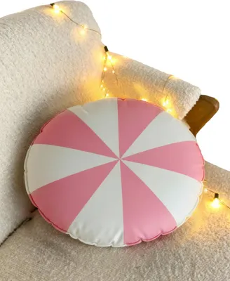 A round pillow with a pink and white striped pattern rests on a textured white surface, possibly a chair or sofa. String lights with warm yellow bulbs are draped around the pillow and the surface.