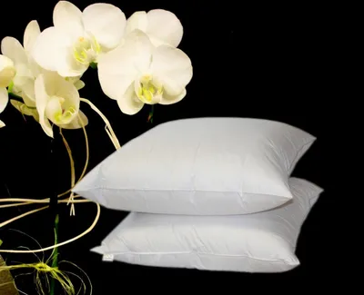 Two white pillows are stacked on top of each other, with white orchids in the background.