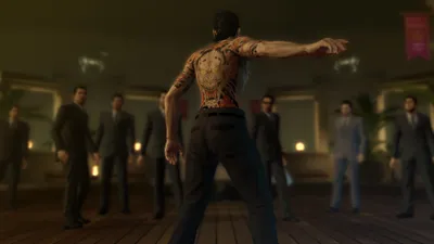 A group of men in suits stand around a man with a large tattoo on his back.