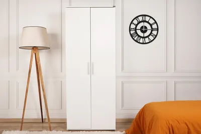 A white wardrobe in a room with a floor lamp and a bed.
