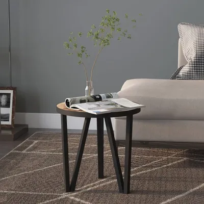 A round side table with a magazine and a vase with branches on it, placed on a rug next to a sofa.