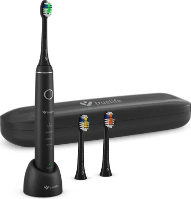 A black electric toothbrush with its charging base and two replacement brush heads, placed in front of a black carrying case.