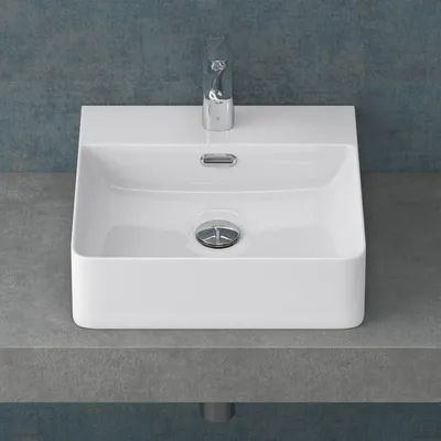 A white ceramic sink with a chrome faucet and drain, placed on a gray countertop against a blue textured wall.