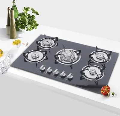 A gas cooktop with five burners is shown on a white countertop, with some kitchen accessories in the background.