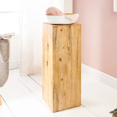 A wooden pedestal with a bowl of yarn on top, placed near a window with sheer curtains and a pink wall in the background.