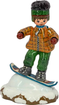 Ein fröhliches Winterkind mit roter Jacke und grüner Hose steht auf einem Snowboard und gleitet über einen schneebedeckten Hügel während es eine graue Mütze mit Bommel trägt und seine Arme ausbalanciert.