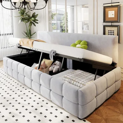A light gray upholstered sofa bed with its storage compartment open, revealing stored items like pillows and a stuffed bunny. The bed is partially extended.