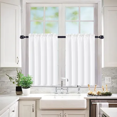 A kitchen sink area with white curtains hanging over a window.