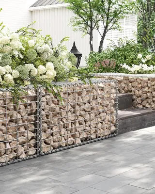 A gabion wall with stones and plants in a garden setting.