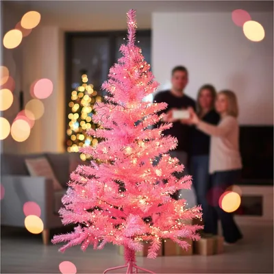 A family is gathered around a pink Christmas tree, with another decorated tree in the background.
