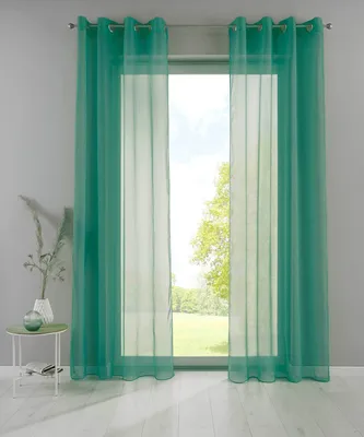 A pair of teal sheer curtains hanging in front of a window overlooking a garden.