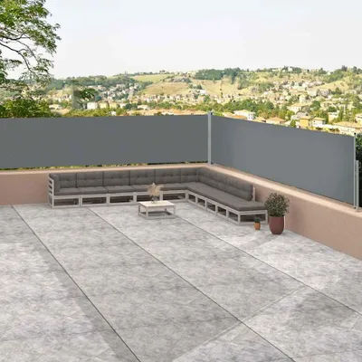 A patio with a sectional sofa and a retractable side awning, overlooking a town on a hillside.