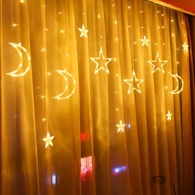 A string of LED lights shaped like moons and stars hanging on a yellow curtain.