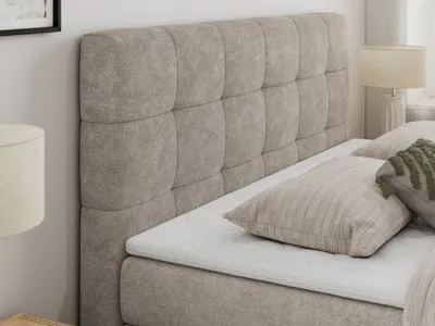 A close-up view of a beige upholstered bed with a tufted headboard and pillows.