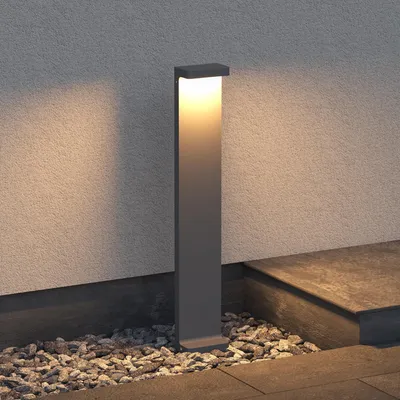 A modern outdoor lamp stands on gravel next to a textured wall and stone steps.