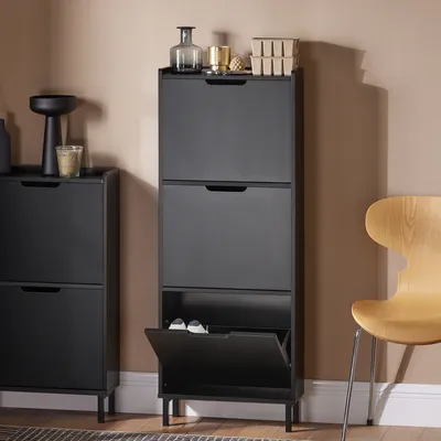 A black shoe cabinet with multiple flip-down compartments, placed next to another similar cabinet and a wooden chair.