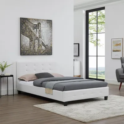 A white upholstered bed frame with a mattress and bedding is shown in a bedroom setting with a large window in the background.