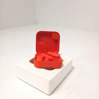 A pair of red wireless earbuds in their open charging case, placed on a white stand.