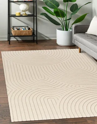A modern rug with a geometric pattern is placed on a wooden floor in a living room setting, next to a sofa and a plant.