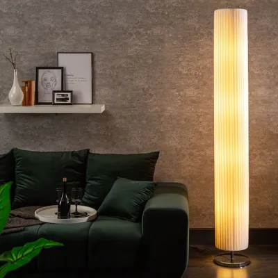 A living room scene with a sofa, a floor lamp, and a shelf with decorative items.