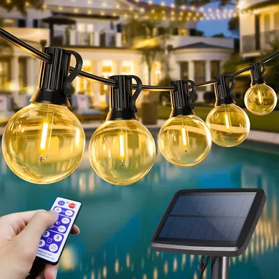 A string of globe-shaped LED lights hangs over a swimming pool at dusk, with a hand holding a remote control and a solar panel visible in the foreground.