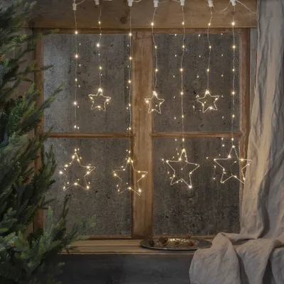 A window decorated with star-shaped string lights, with a Christmas tree branch visible on the left.