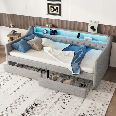 A gray upholstered daybed with storage drawers, set up in a bedroom with decorative pillows and blankets.