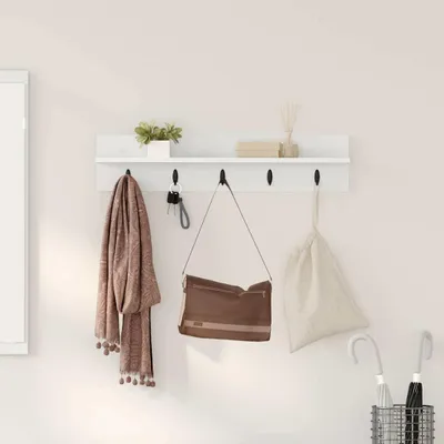 A white shelf with hooks mounted on a light-colored wall, displaying various items like a scarf, a handbag, keys, a plant, books, and a vase with reeds. Umbrellas are in a basket below.