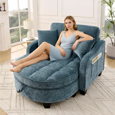 A woman is sitting on a blue sofa with a chaise lounge in a living room setting.