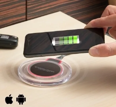 A hand is holding a smartphone over a wireless charging pad on a wooden surface.