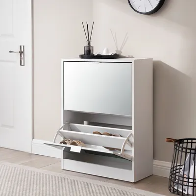 A white shoe cabinet with a mirrored front is shown in a room with a white door and a rug.