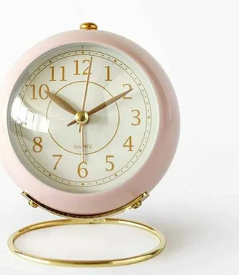 A close-up studio shot of a pink analog alarm clock with gold accents.