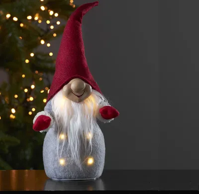 A festive gnome decoration with lights, set against a blurred Christmas tree background.