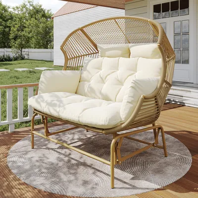 A two-person hanging chair with cream cushions sits on a wooden deck, with a lawn and house in the background.