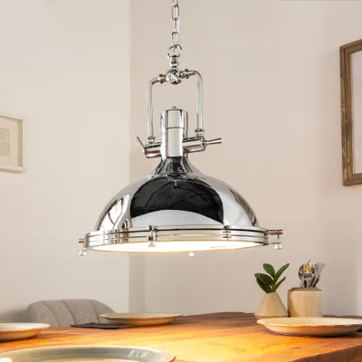 A chrome pendant light hangs over a wooden dining table set with plates.