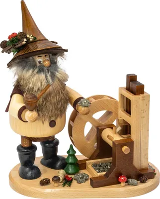 Ein Erzwichtel mit spitzem Hut und Pfeife steht neben einem detailreichen Pochwerk aus Holz und ist von kleinen Dekorationen wie einem Tannenbaum und Pilzen umgeben