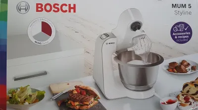 The image shows the packaging of a Bosch MUM5 Styleline kitchen machine, with a picture of the machine and some food items on the box.