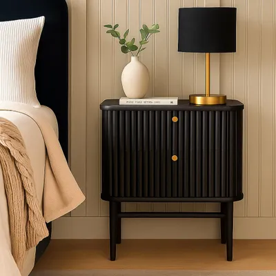 A black fluted nightstand next to a bed with a beige throw blanket.