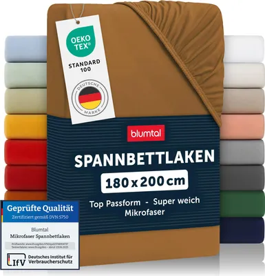 A product shot of a brown fitted sheet, with multiple other fitted sheets of different colors stacked on the left and right sides. Several tags and labels are attached to the main product.