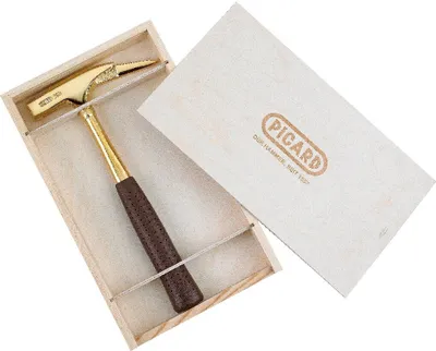A gold-plated hammer with a brown handle is displayed in a wooden box, with the lid open and resting beside it. The lid has the brand name 'PICARD' embossed on it.