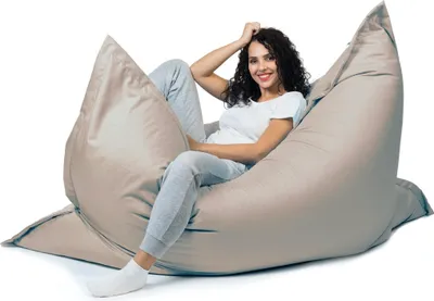 A woman is sitting comfortably on a large, light gray beanbag chair.