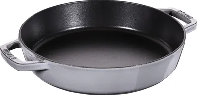 A Staub cast iron frying pan with two handles is shown from a diagonal, slightly elevated angle against a white background.