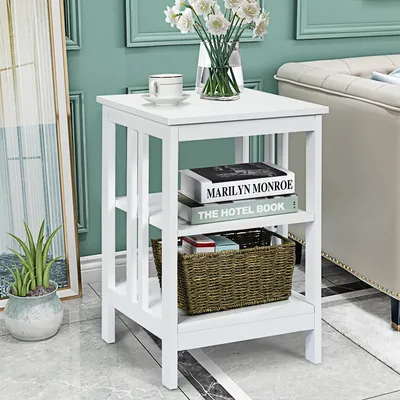 A white three-tiered side table with books and a basket on it, placed next to a sofa and a potted plant.