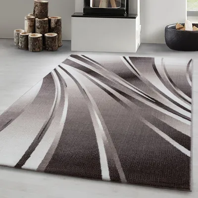 A modern abstract wave design rug in shades of gray and white is shown on a light gray floor, with a fireplace and stacked logs in the background.