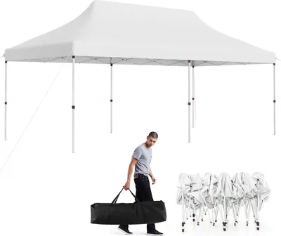 A man carries a folded tent bag next to a set-up tent.