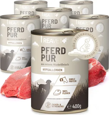 Several cans of dog food are arranged with raw meat in front of them.