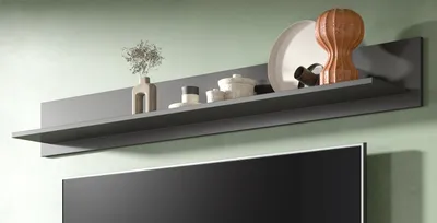A gray floating shelf mounted on a light green wall above a television, displaying various decorative items.