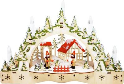 A wooden Christmas decoration depicting a winter scene with a house, trees, and figures.